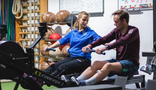 Ein Bild eines Mitglieds beim Training auf dem Rudergerät unter Anleitung eines Coaches